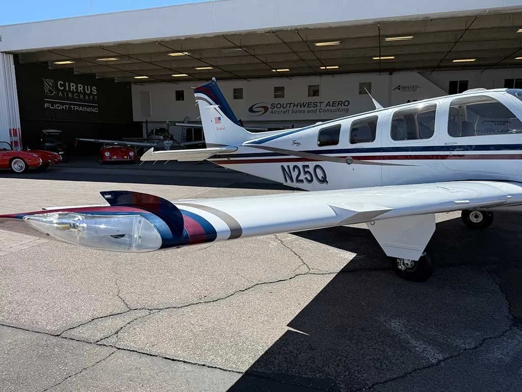 A close-up view of the tail and right wing of the white Beechcraft Bonanza A36, registration N25Q, showing its blue and red stripe paint scheme.