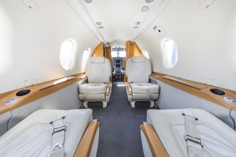 The interior of a Pilatus PC-12 aircraft with white leather seats and fold-out tables.