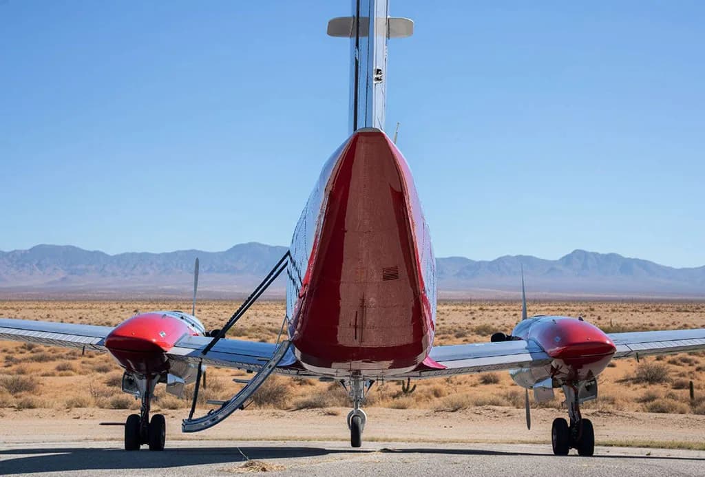 Rear view of a red and silver Beechcraft King Air N350FC with its passenger door open, parked on an airfield.