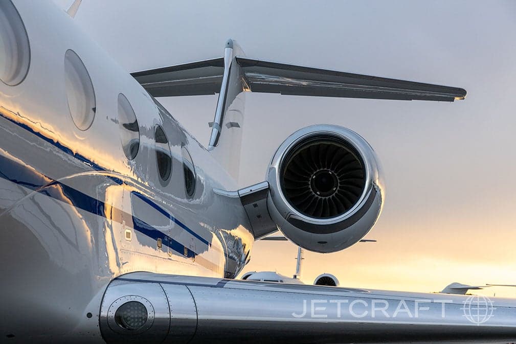 A close-up view of the engine and tail section of a white Gulfstream G550 business jet reflecting the sunset.