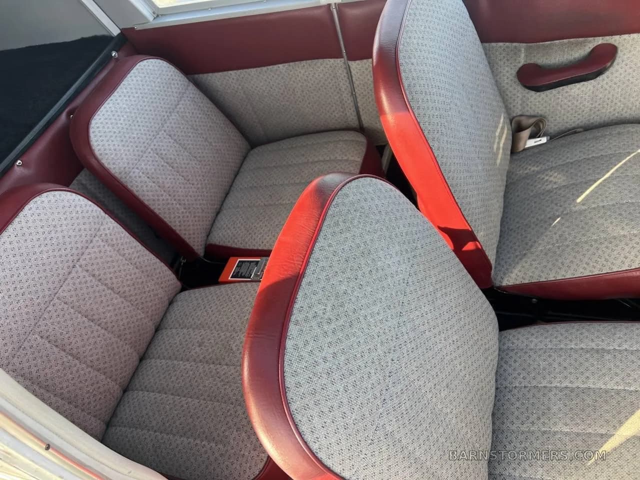 The interior cabin of a small aircraft, showing two rear seats with red and patterned fabric.