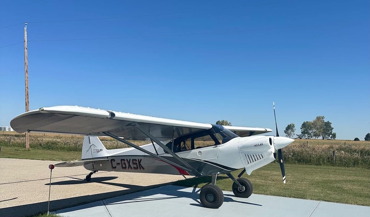 A side view of a white, grey, and red CubCrafters XCub aircraft (C-GXSK) parked on an airfield.
