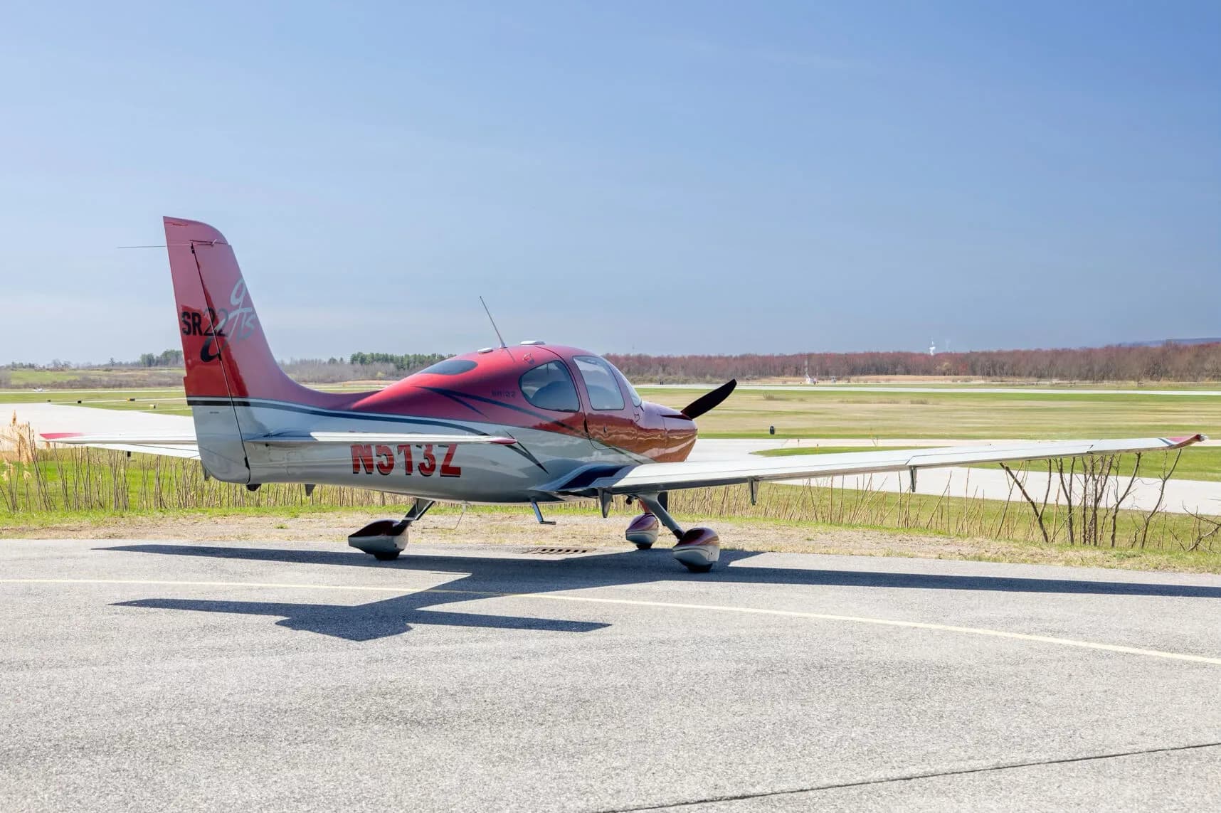 Three-quarter rear view of the red and grey Cirrus SR22T aircraft (N513Z) on an asphalt runway.