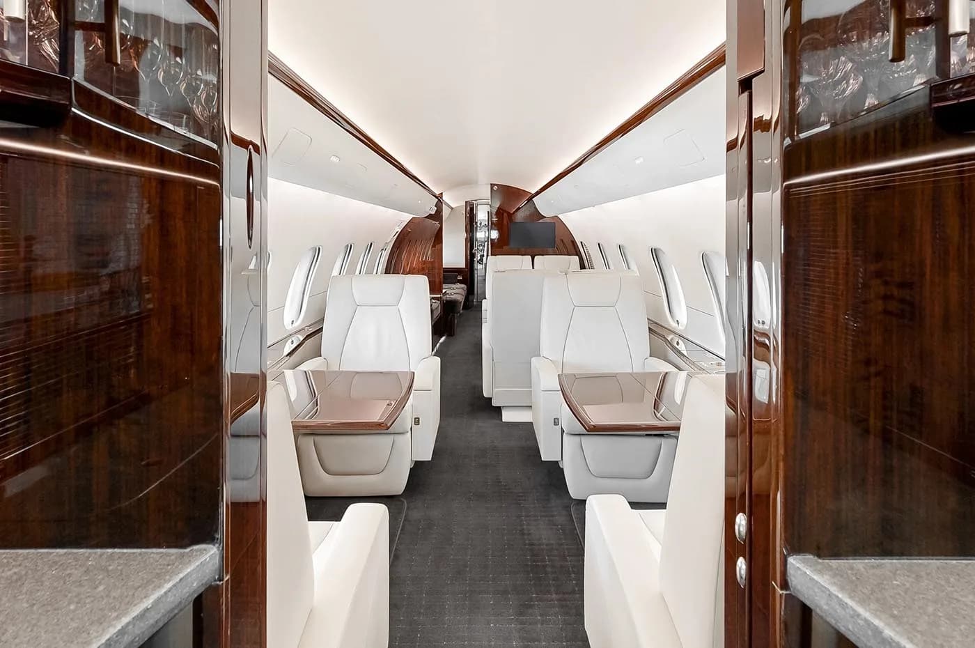 A view through the business jet's cabin, showing cream leather seats, dark wood tables, and a spacious aisle.