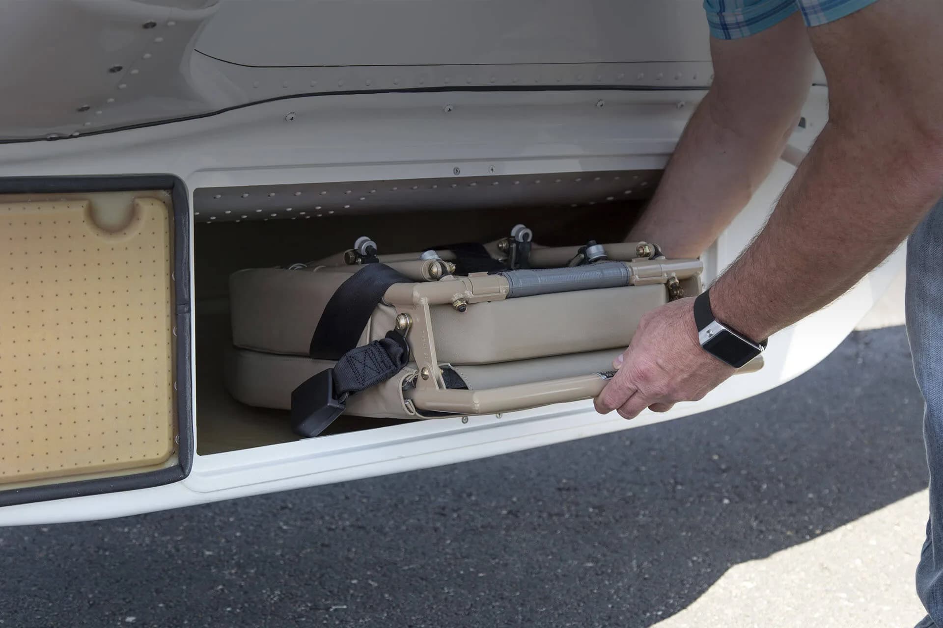 A person loading a folded seat into the storage compartment of a Cessna Stationair.