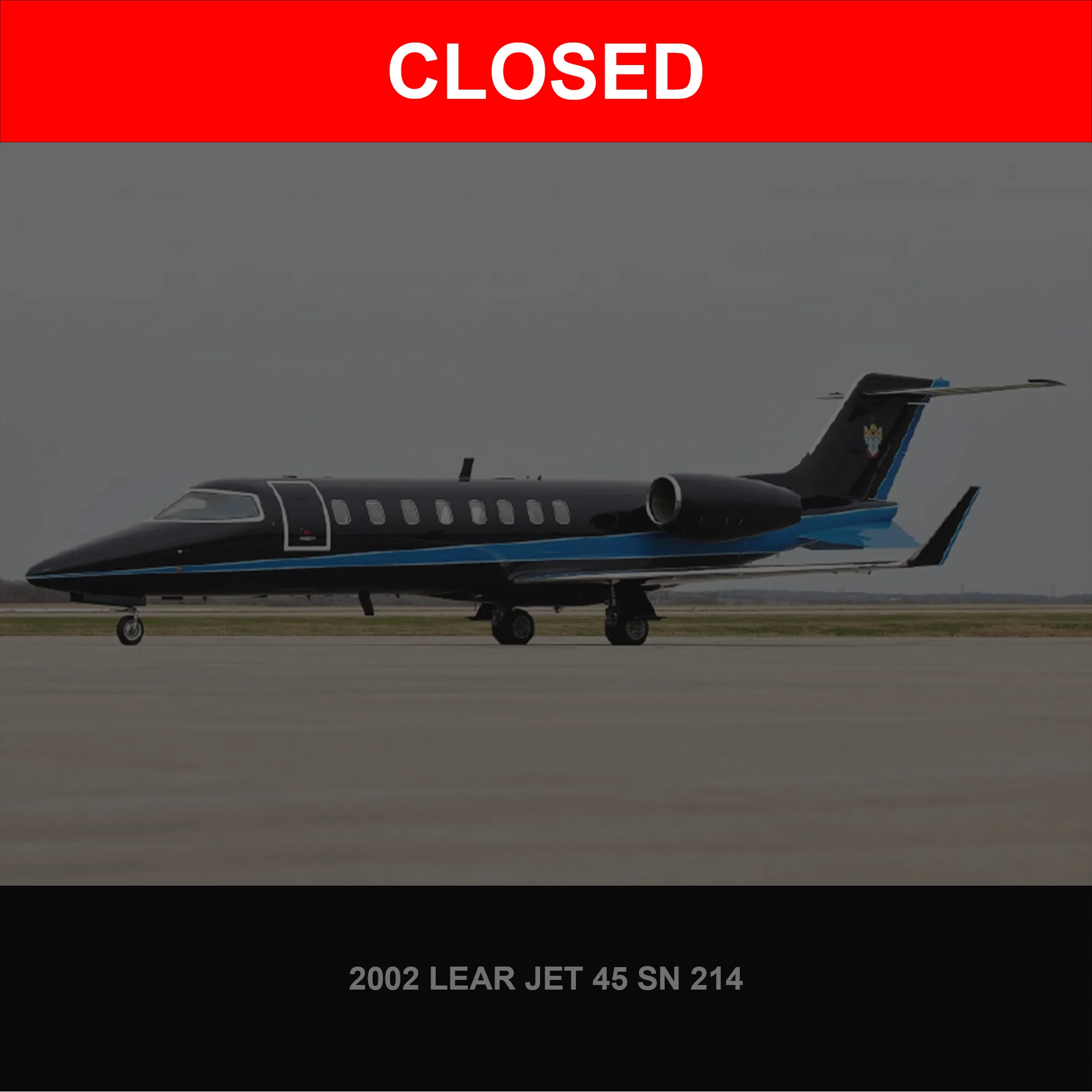 A black Learjet 45 with blue stripes on the fuselage and tail is parked on an asphalt runway under an overcast sky.