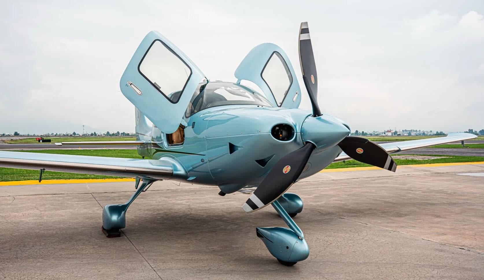 Front-right view of a light blue Cirrus SR22T aircraft with its gull-wing doors open on an airfield.
