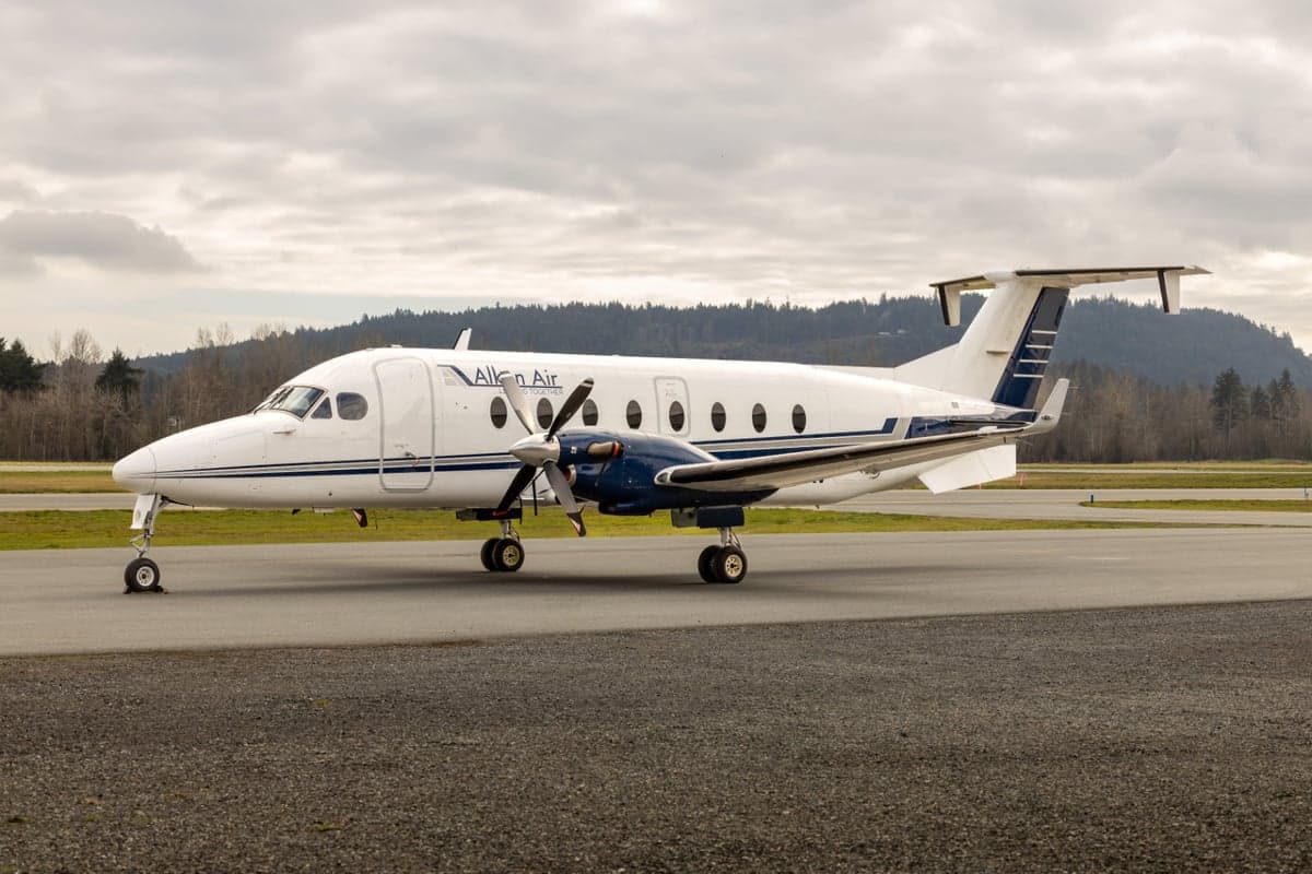 Aerial view of a Beechcraft 1900C in a light gray paint scheme on the tarmac.
