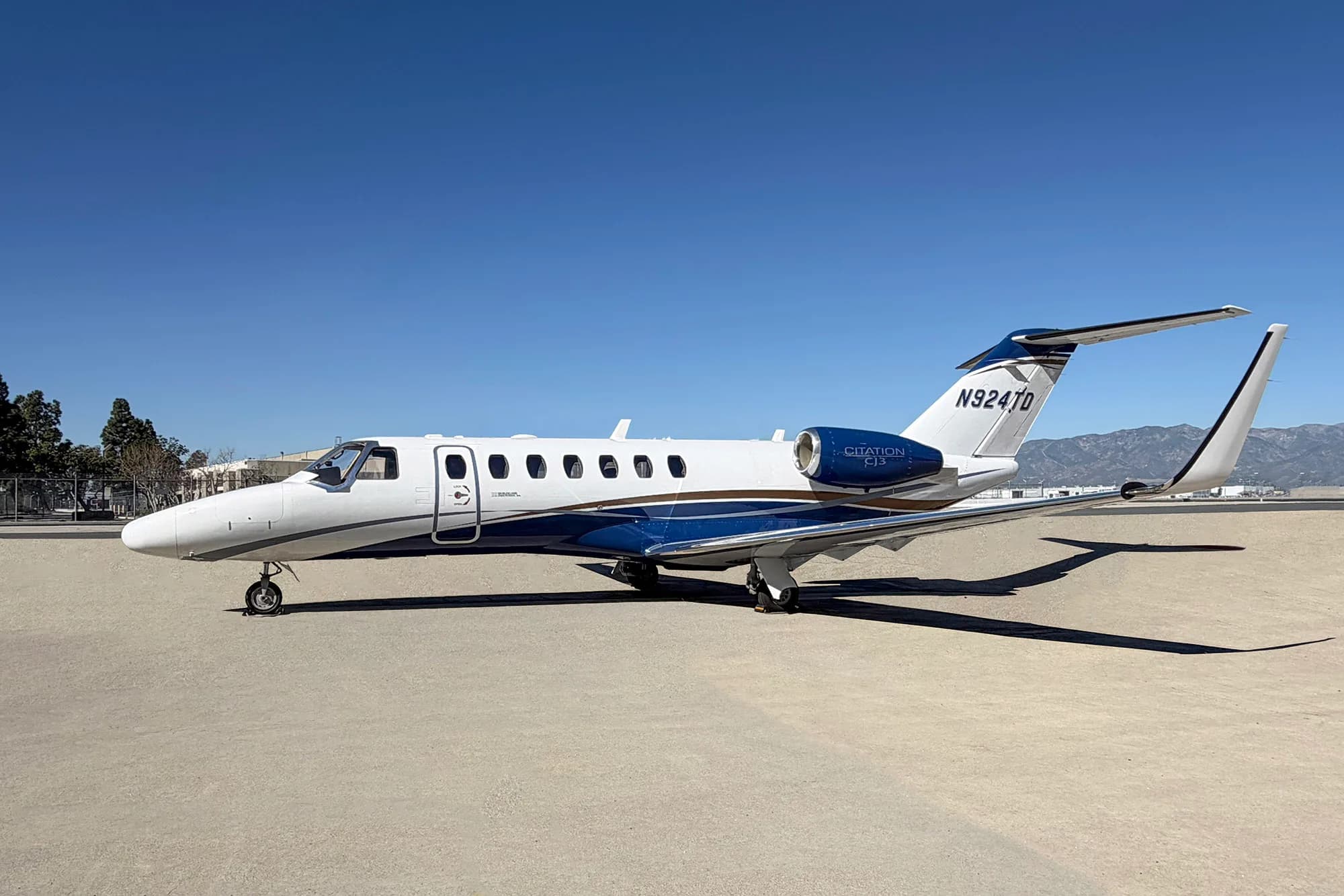 A white and blue Cessna Citation CJ3 private jet with registration N924TD is parked on a tarmac under a clear blue sky.