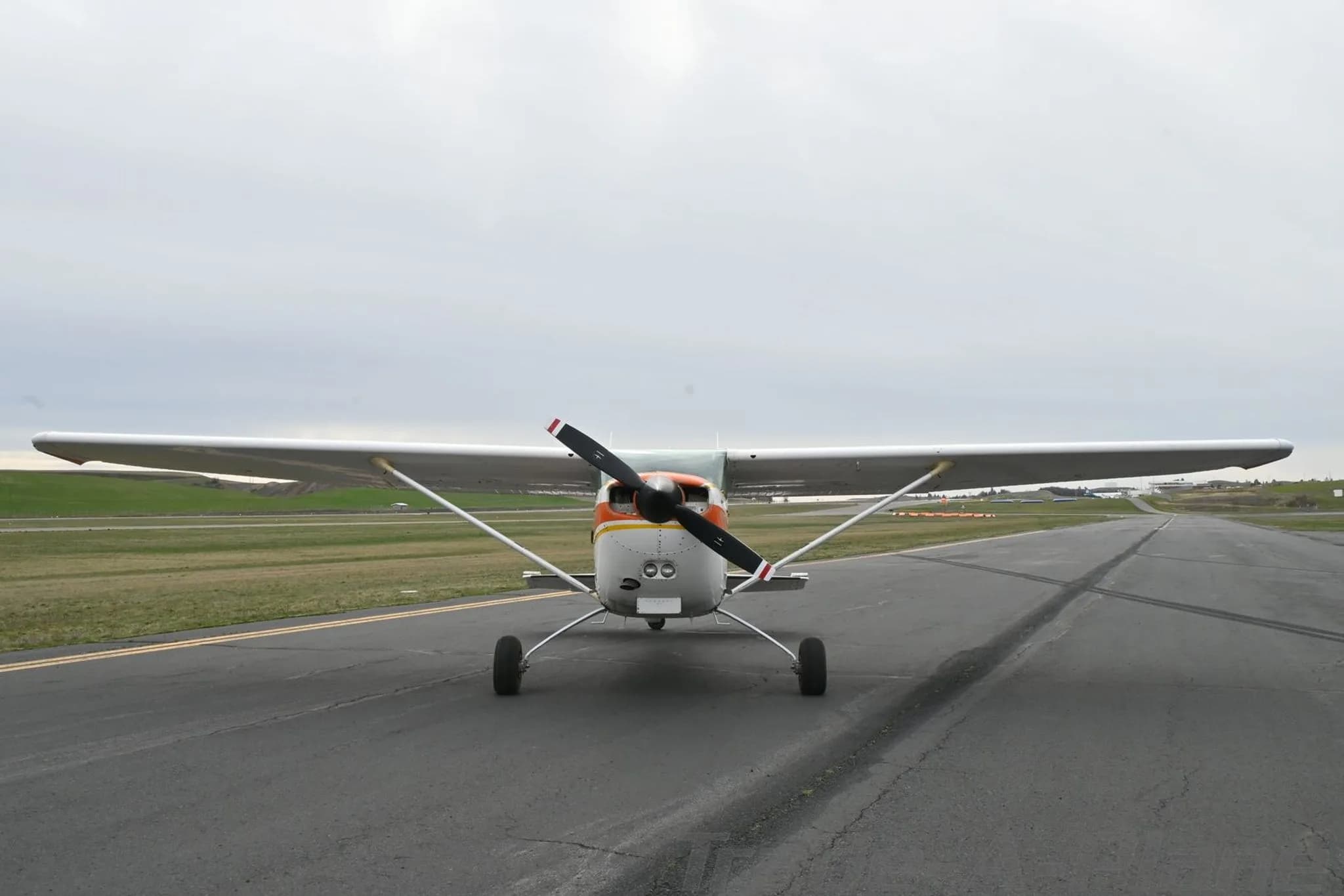 A white and orange Cessna 172 Hawk XP II (N5205V) parked on an airfield, viewed from the front.