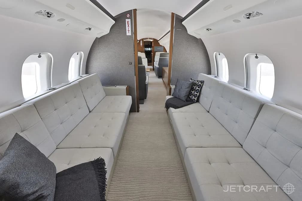 The aft cabin of a Bombardier Global 6000, featuring two long, light grey fabric sofas facing each other.