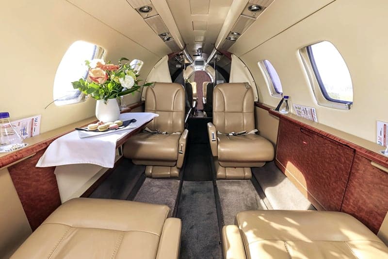 View of the aircraft cabin with tan leather seats and a table with flowers.