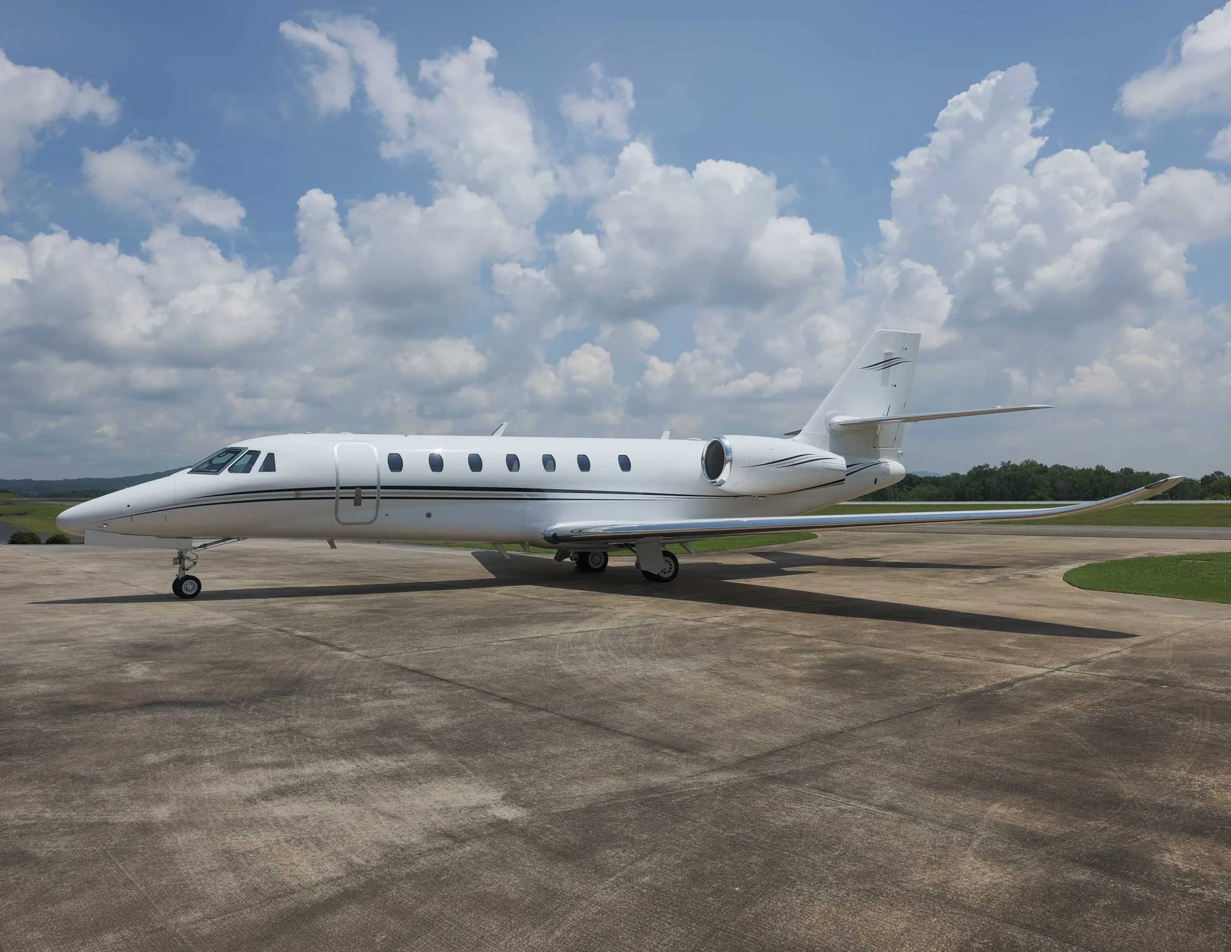A white business jet with black stripes parked on an airfield, casting a shadow on the concrete.