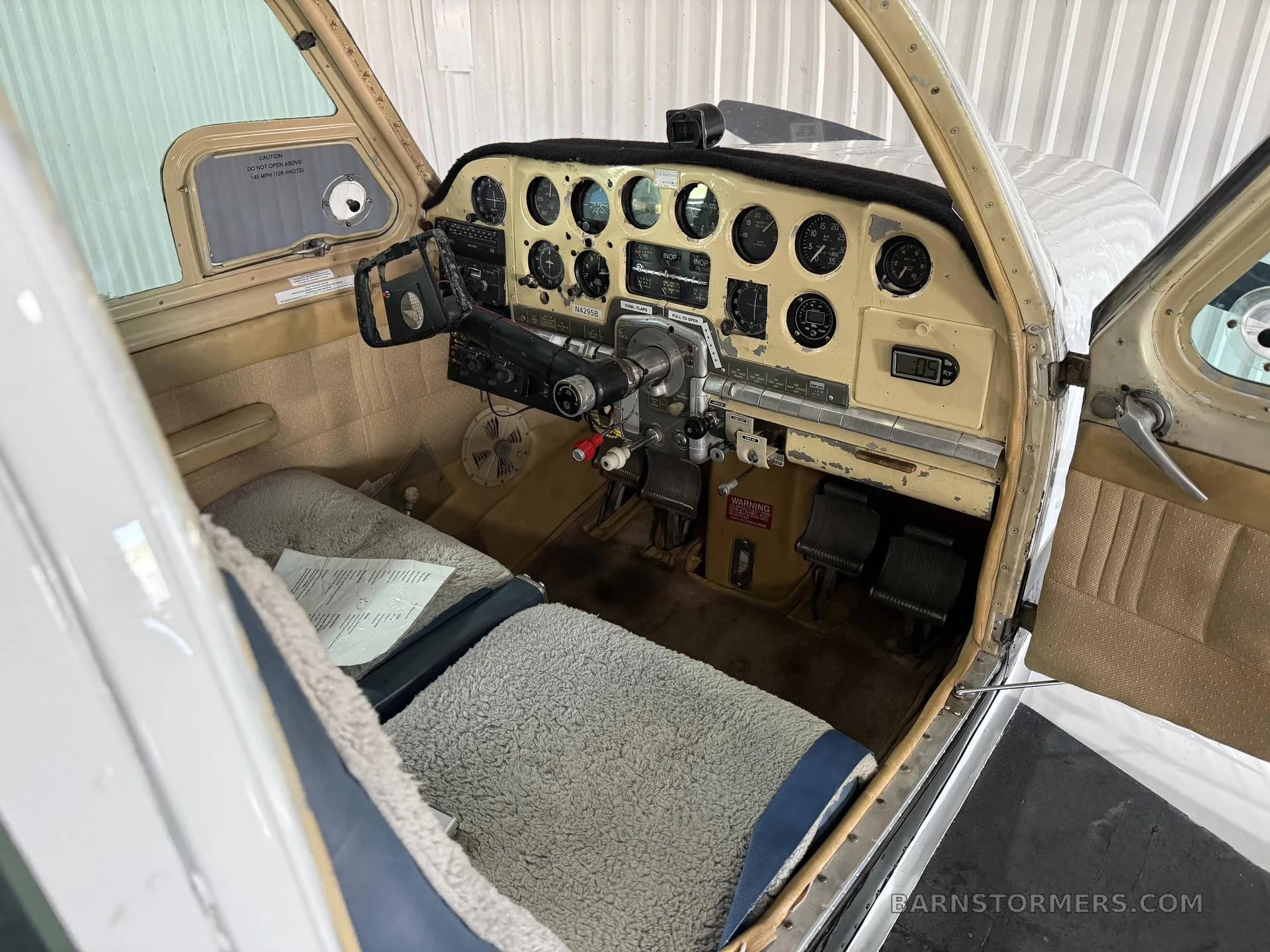 The cockpit of a small aircraft with a beige instrument panel, dual yokes, and sheepskin seat covers.