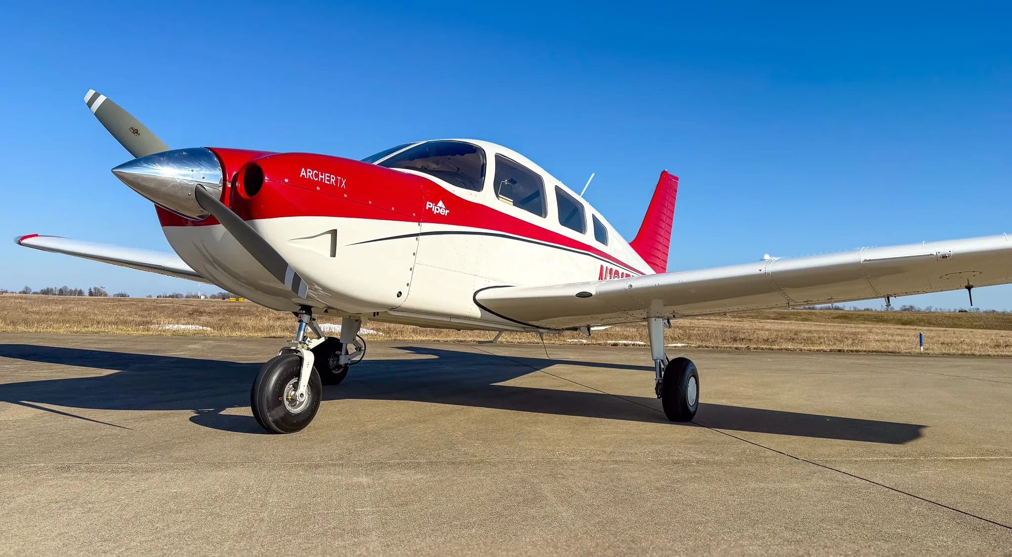 A front-left view of a red and white Piper Archer TX aircraft, tail number N161TF, parked on an asphalt tarmac.