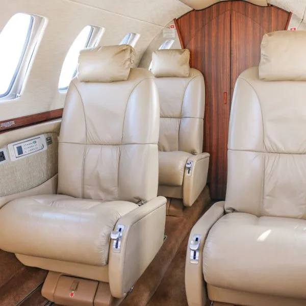 Angled interior view of an aircraft cabin showing beige leather seats and windows.