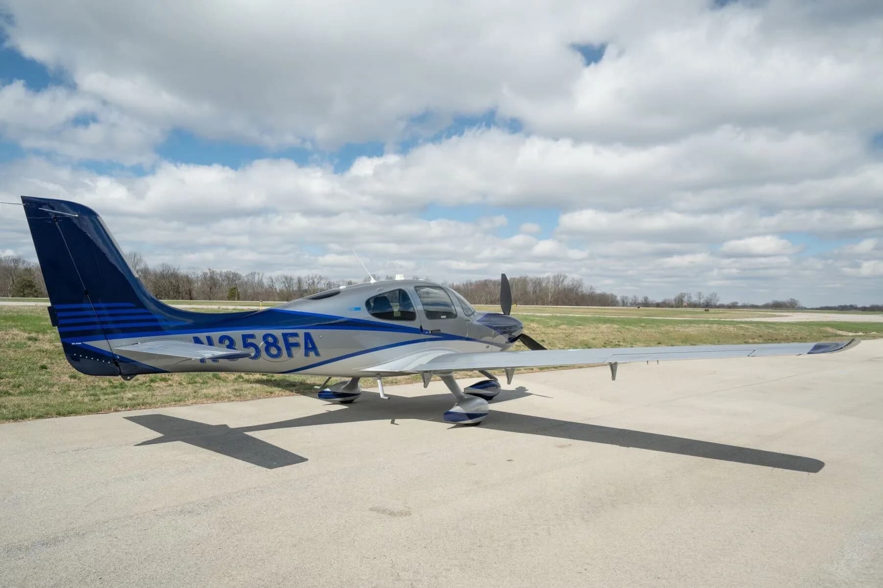 A silver and blue Cirrus SR22T aircraft, registration N358FA, parked on an airfield with its doors closed.