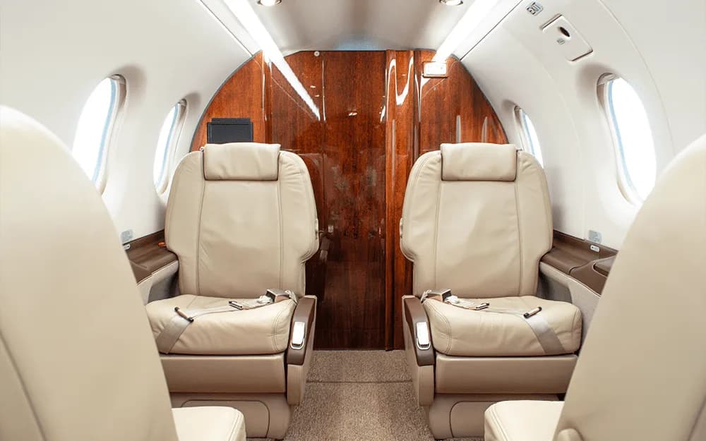 Interior view of a private aircraft cabin showing two rows of beige leather passenger seats.