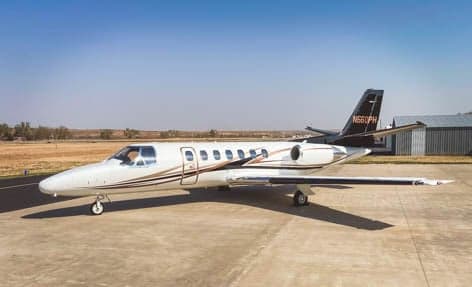 A white business jet with black and brown stripes, registration N560PH, parked on an airfield.