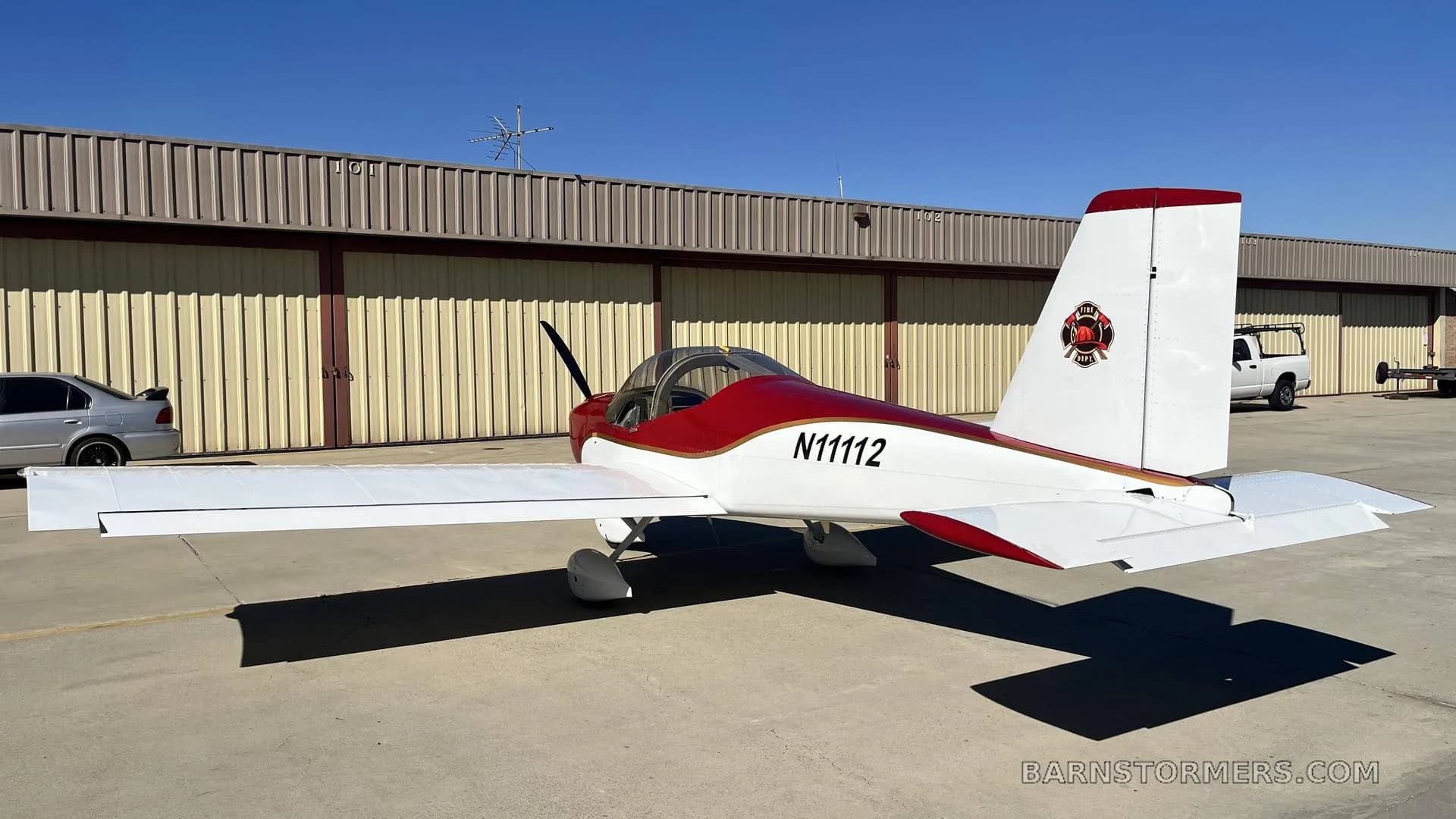A red and white single-engine aircraft with registration N11112 is parked on an airfield apron, viewed from the rear-right.