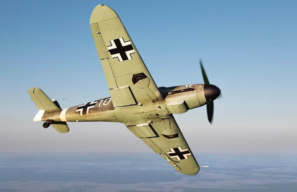 A gray Messerschmitt Bf 109 aircraft in flight against a blue sky.