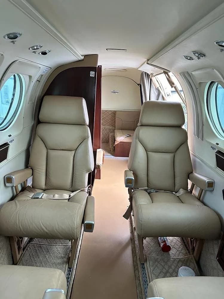 The interior cabin of an aircraft, showing tan leather passenger seats and a view towards the rear compartment.
