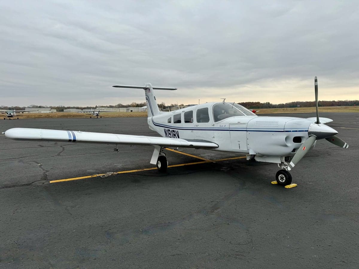 Three-quarter front view of a white single-engine propeller aircraft with blue stripes and registration N191RV on an airfield.