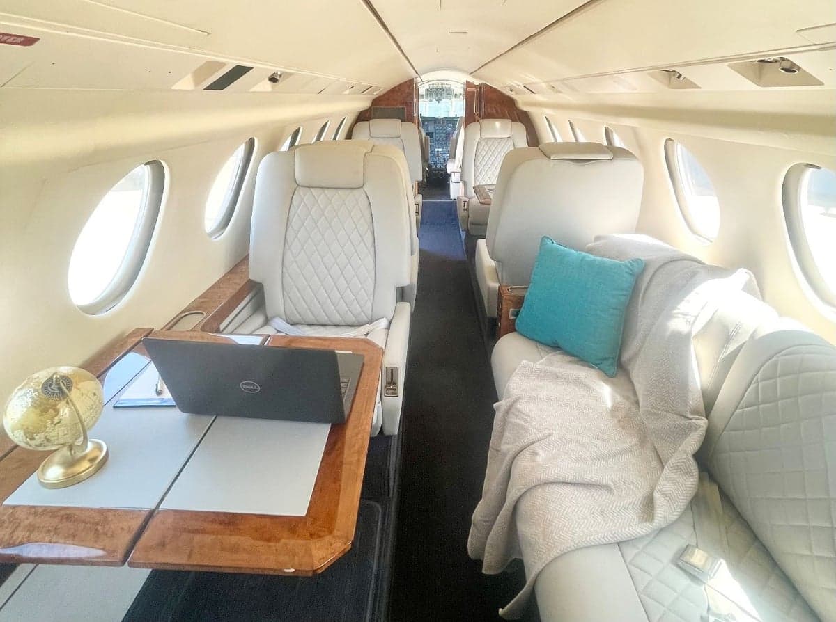 Aircraft interior with white leather seats and a laptop on the table.