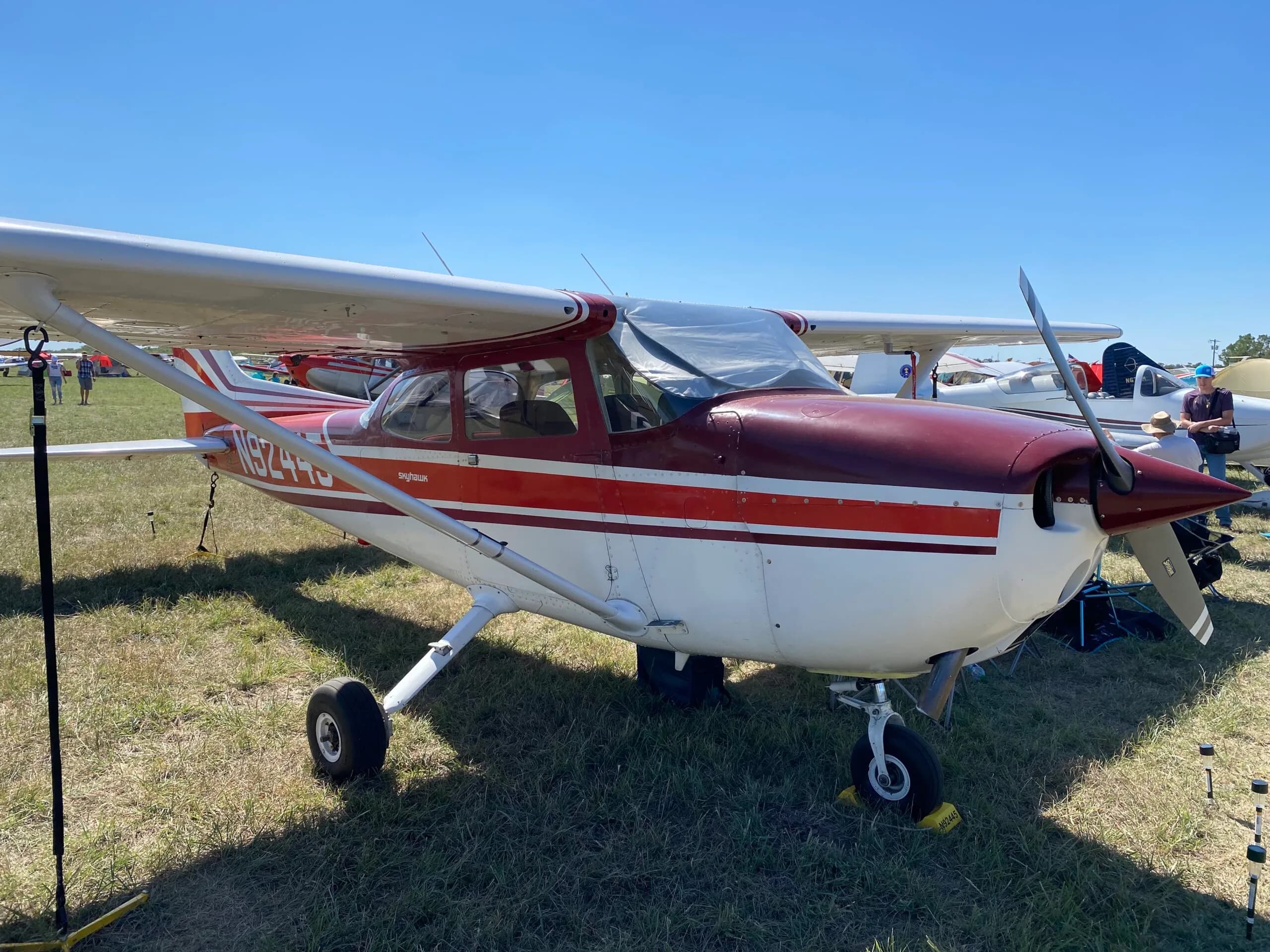 A red and white Cessna Skyhawk (N9244S) is parked on a grassy field under a clear blue sky.