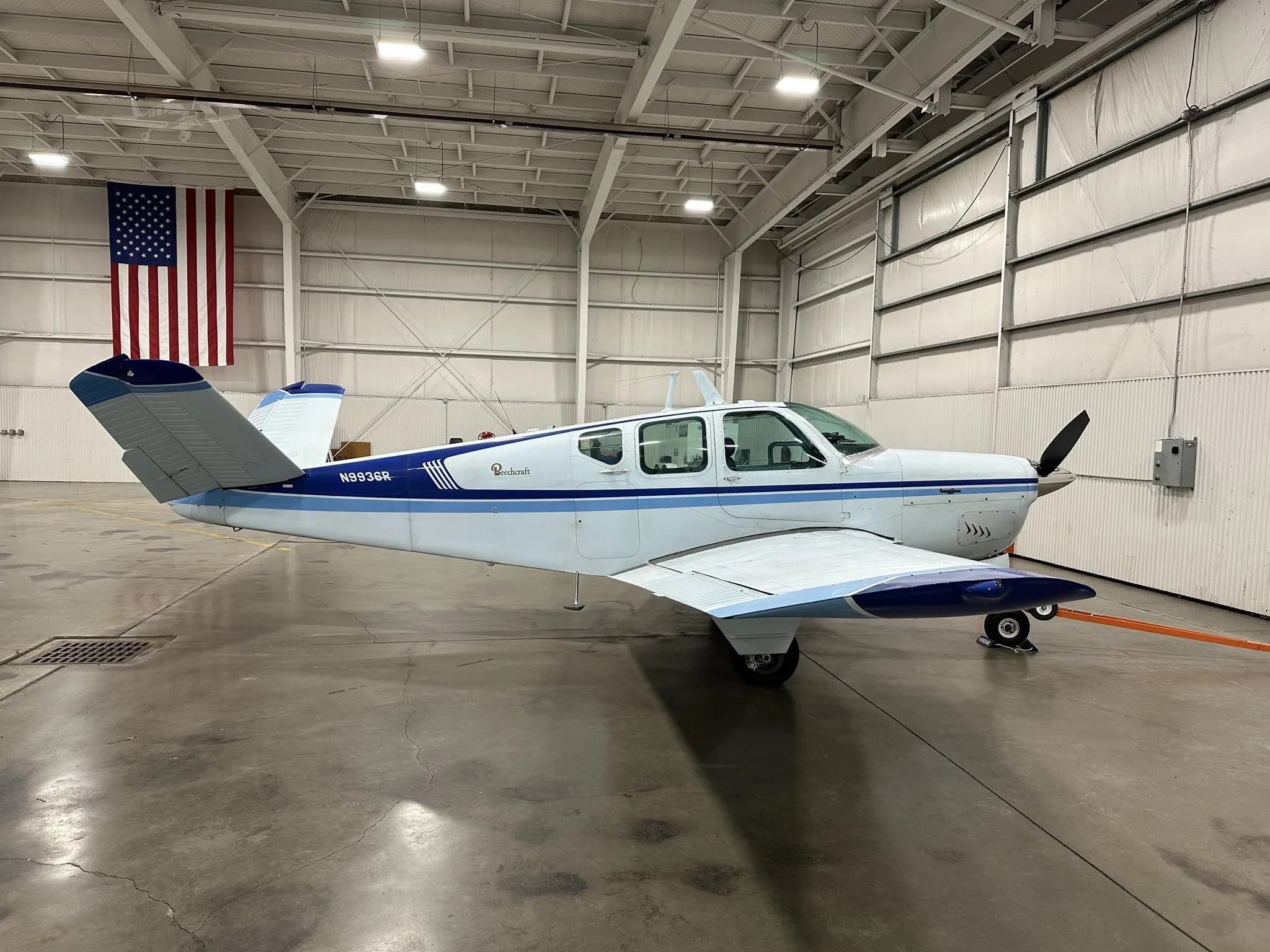 A white and blue Beechcraft Bonanza N9936R parked in a hangar, viewed from the left side.