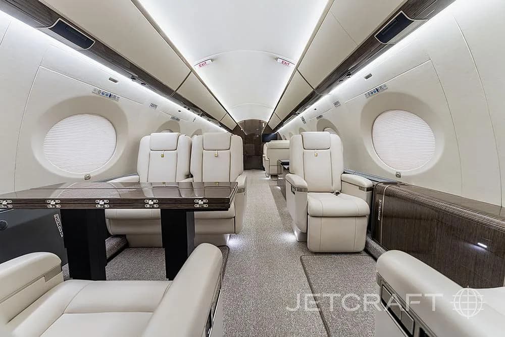 A view inside a private jet cabin, showing cream leather seats arranged around a dark wood table.