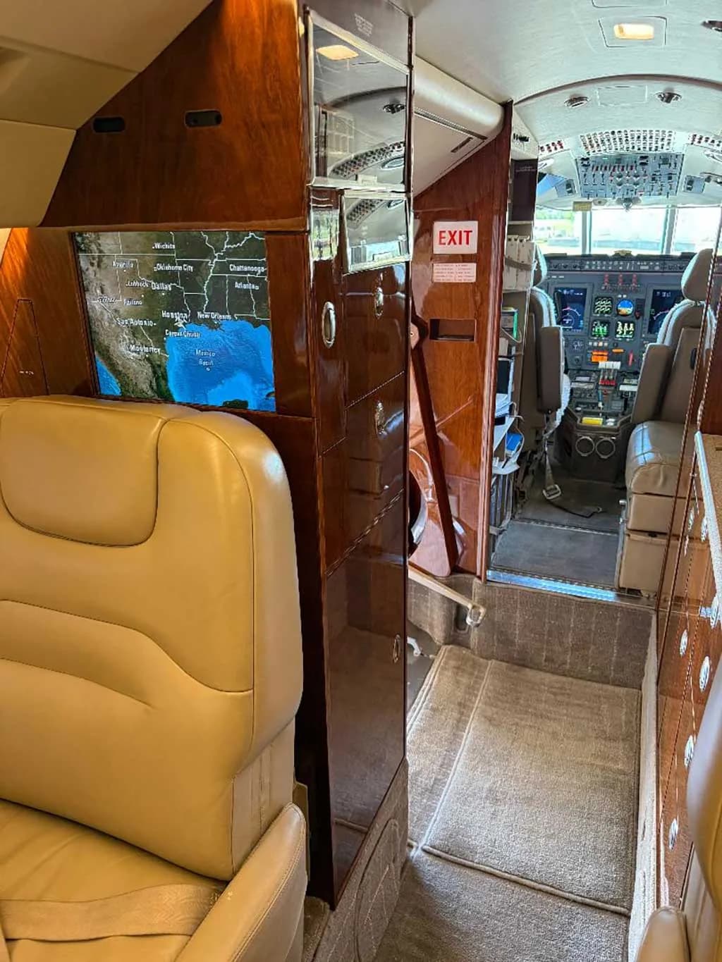 The aircraft cabin looking forward towards the cockpit, with a large display screen showing a map of the United States.