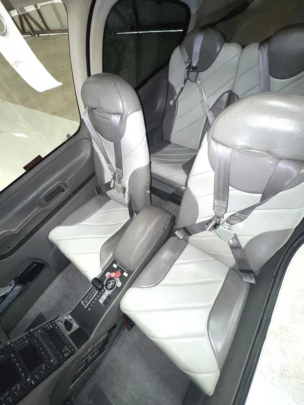 The interior cabin of a Cirrus SR20 aircraft, showing the gray and white leather seats with seatbelts.