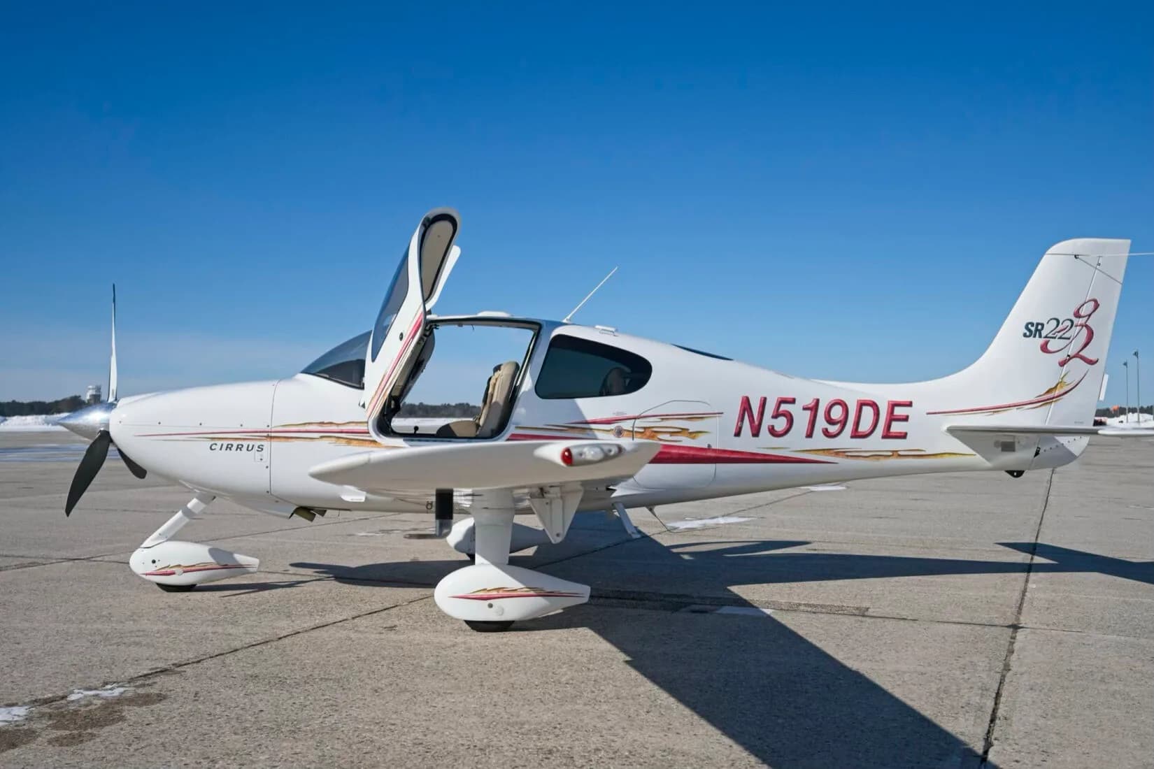 A white Cirrus SR22 aircraft with red and gold decals, registration N519DE, parked on a tarmac with both cabin doors open.