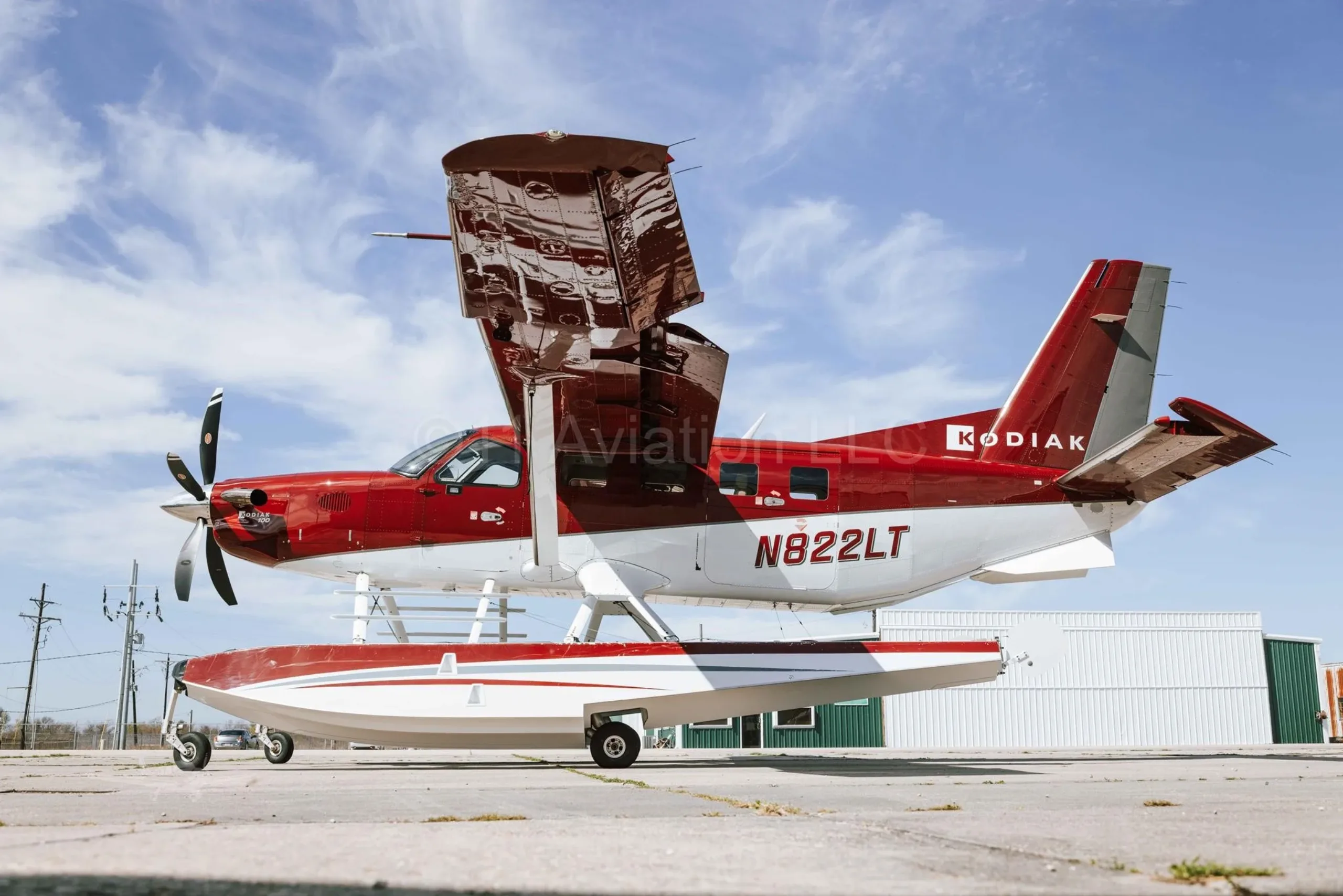 A red and white Kodiak aircraft on floats is parked on the tarmac with its cargo door open.