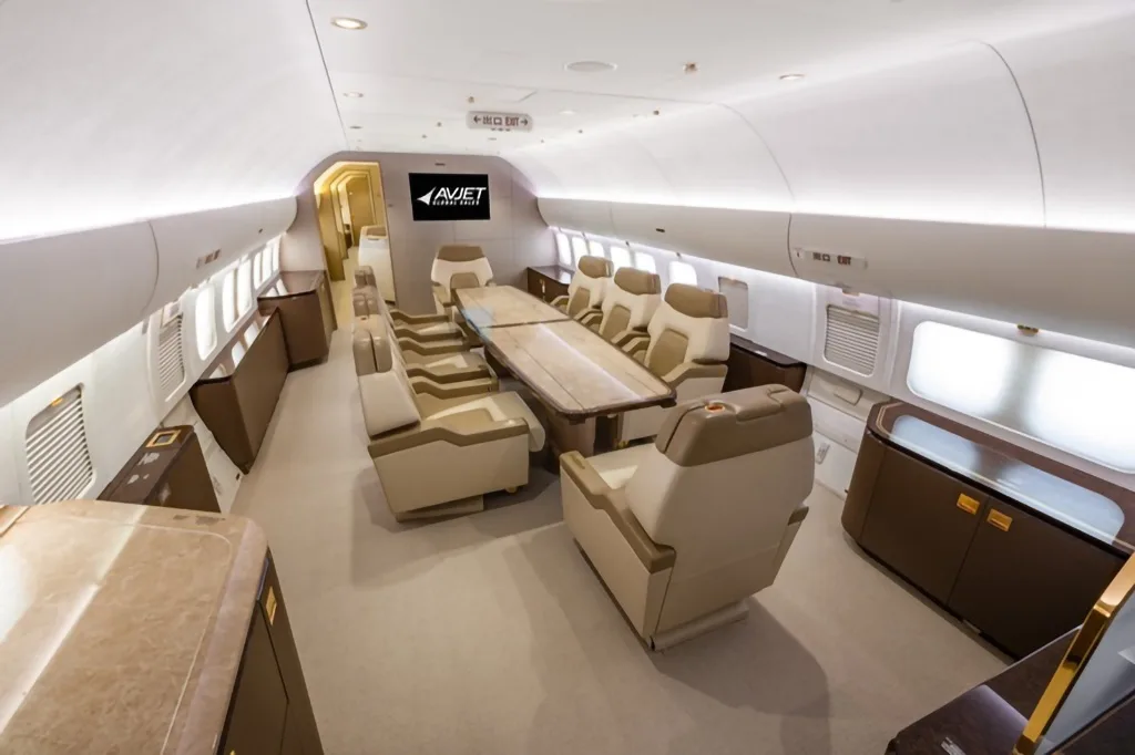 A long dining or conference table surrounded by individual beige leather seats in a luxurious aircraft interior.