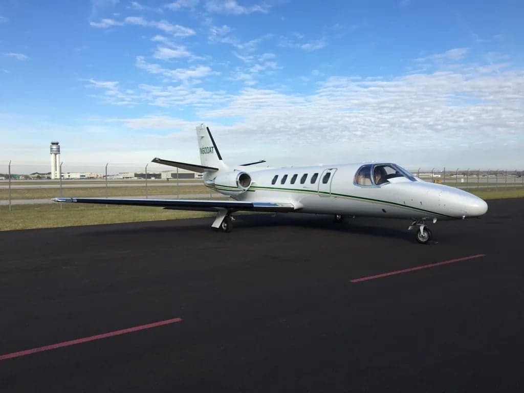 Side view of a white Cessna CitationJet with green stripes on the tarmac.