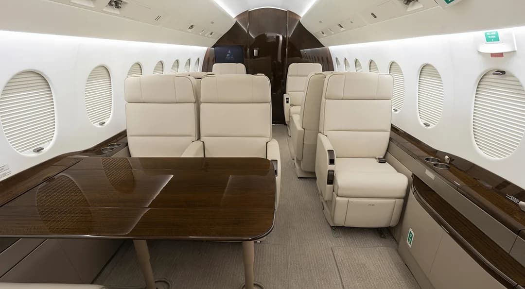 The aircraft interior features cream-colored leather seats and a wood table.