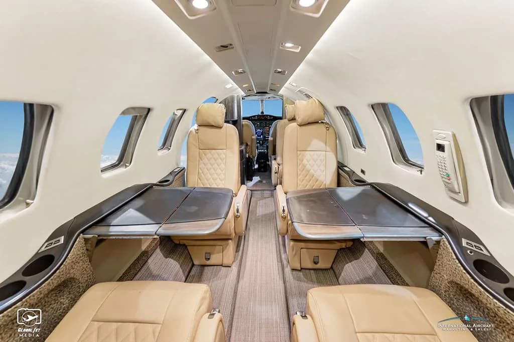The luxurious tan leather interior cabin of a business jet with tables deployed.