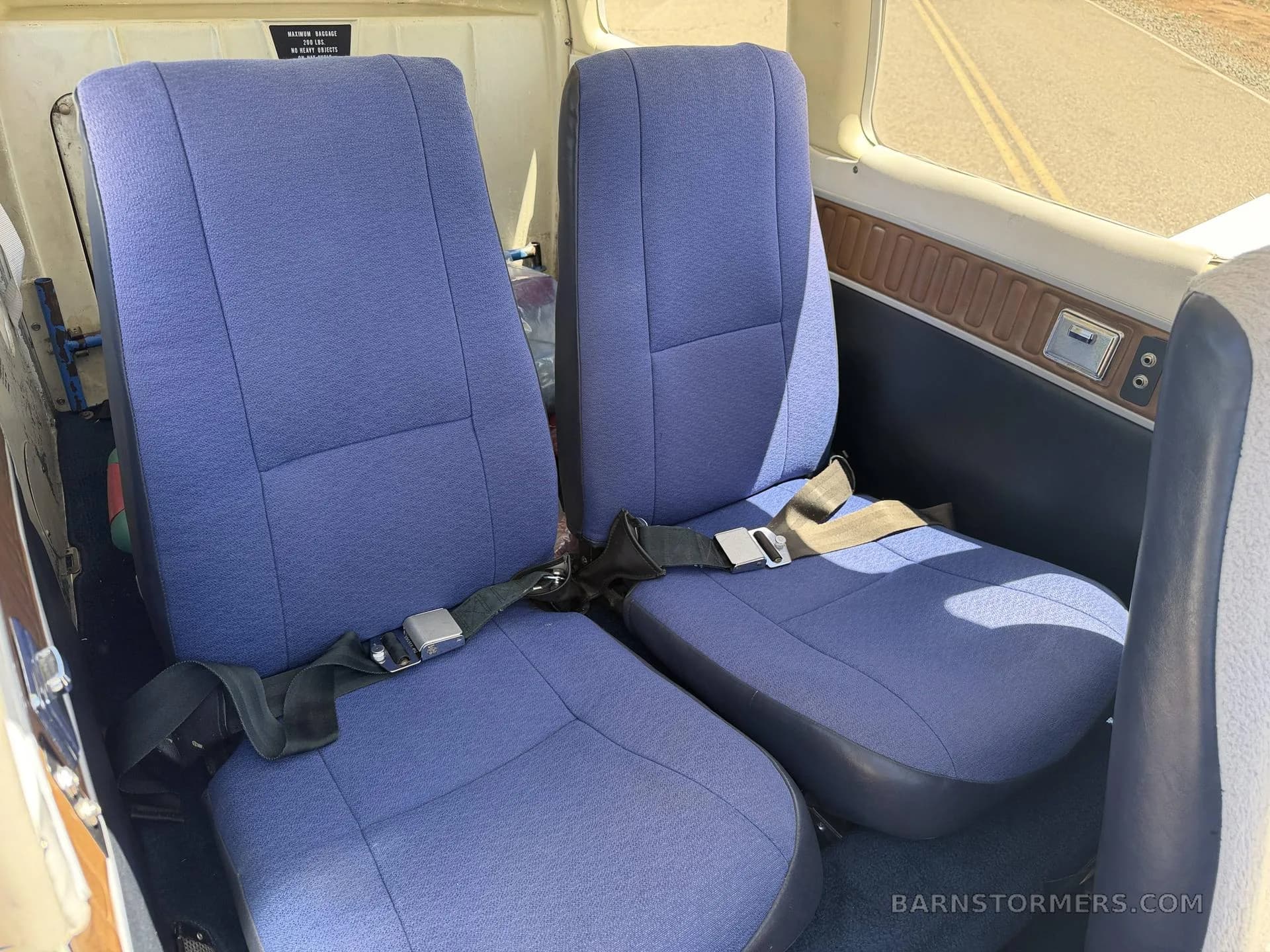 The rear two seats of the aircraft cabin, upholstered in blue fabric, with a window on the right.