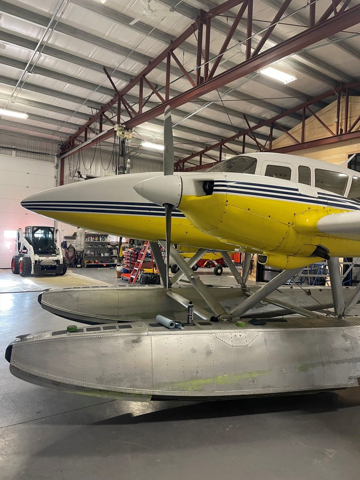 Side view of the yellow and white twin engine aircraft on floats, inside a hangar.