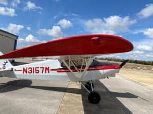 Piper Cub aircraft with red and white paint scheme parked on the tarmac.