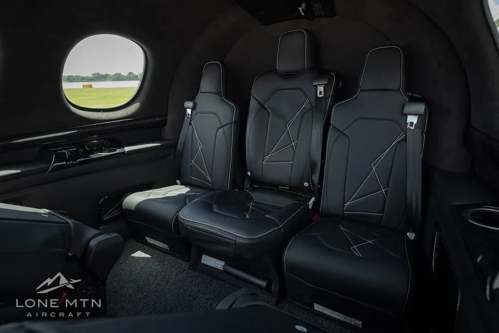 The black leather interior of a Cirrus Vision Jet cabin with three passenger seats and a window view of the tarmac.
