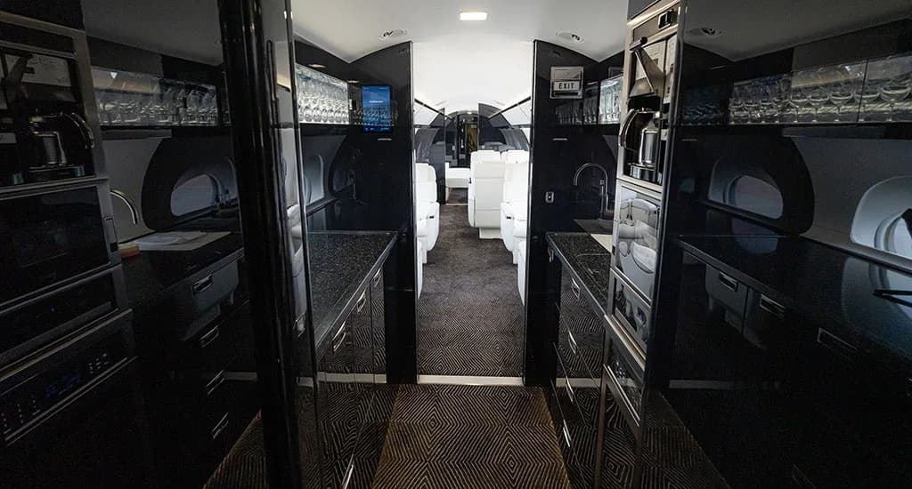 The modern galley of the business jet, featuring black cabinetry, a sink, and glassware storage.