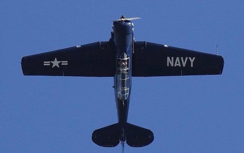 A blue North American T-6 Texan aircraft in flight against a blue sky.