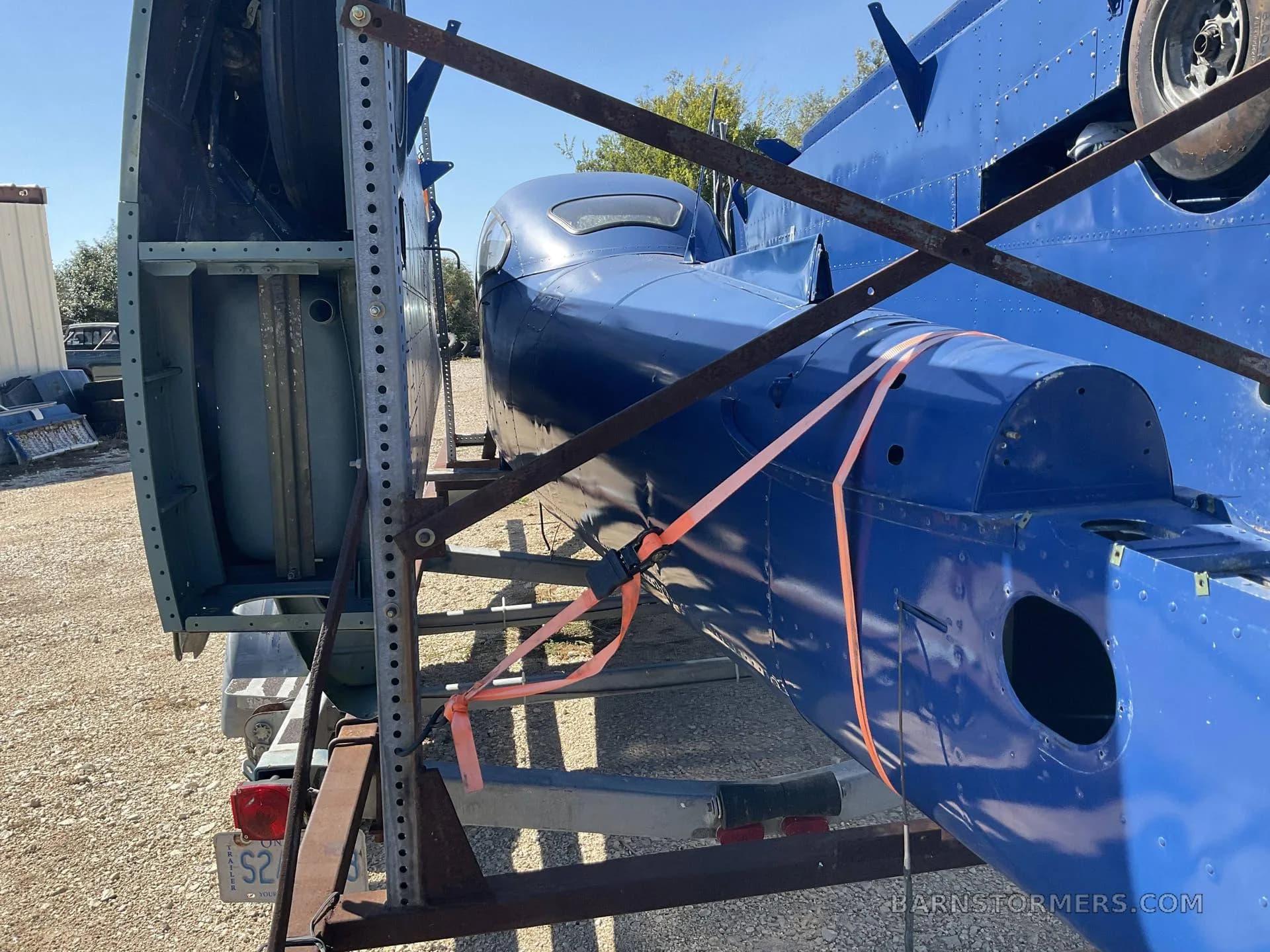 A view of the blue aircraft's rear fuselage and tail section on a trailer, showing the internal structure of the detached vertical stabilizer.