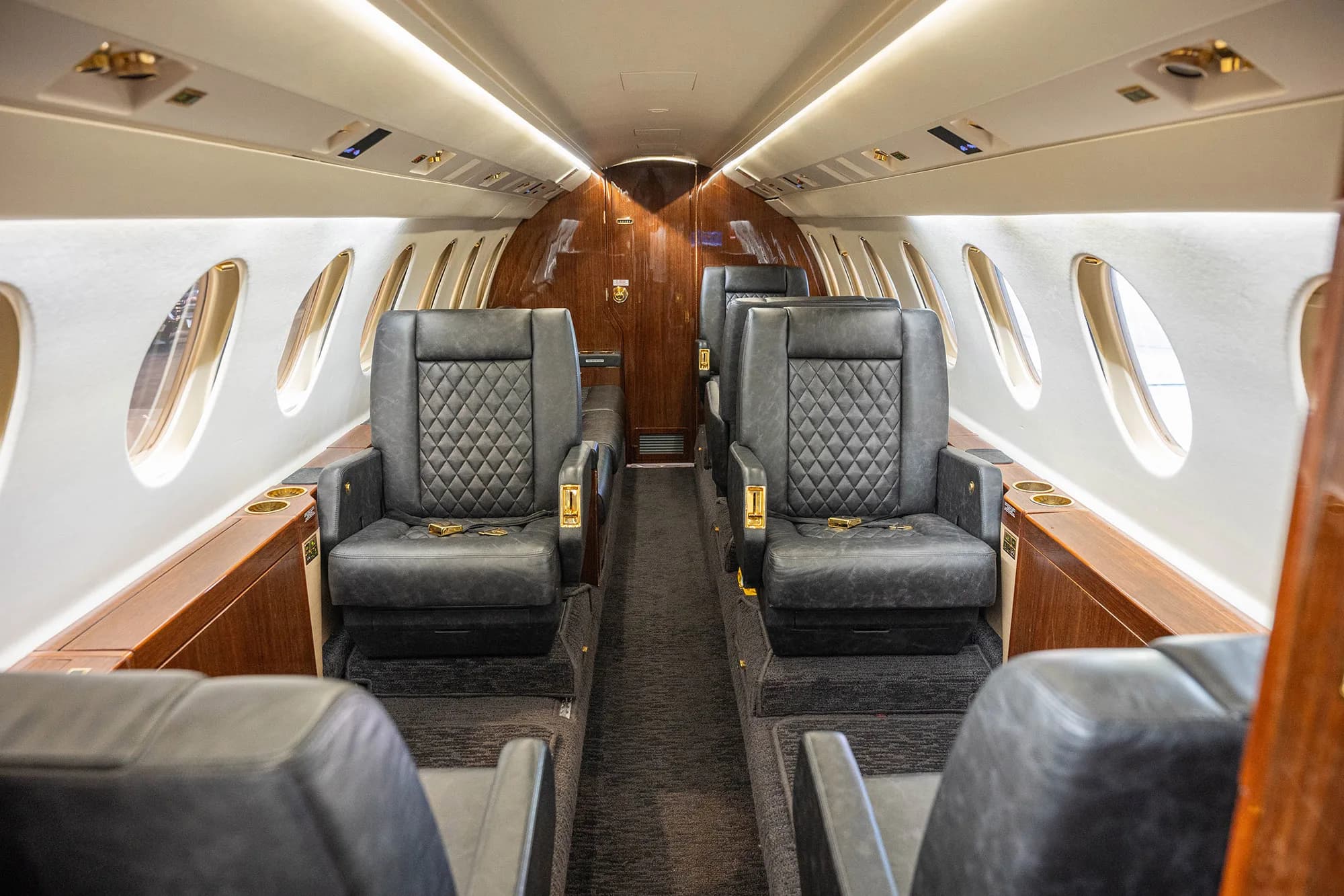 The spacious cabin interior of a Dassault Falcon 900EX business jet with rows of dark quilted leather seats.