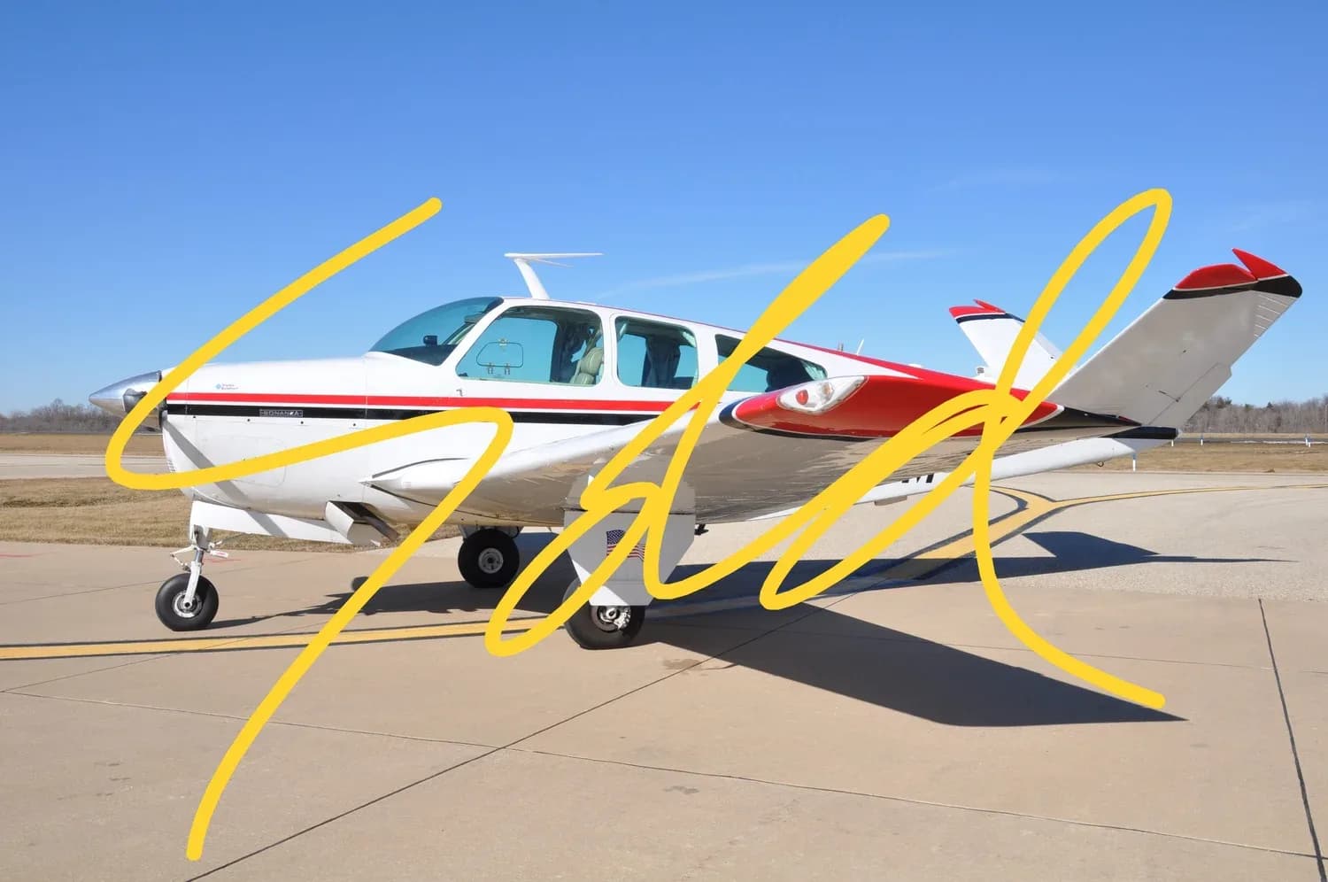A white and red single-engine aircraft is parked on a tarmac under a clear blue sky.
