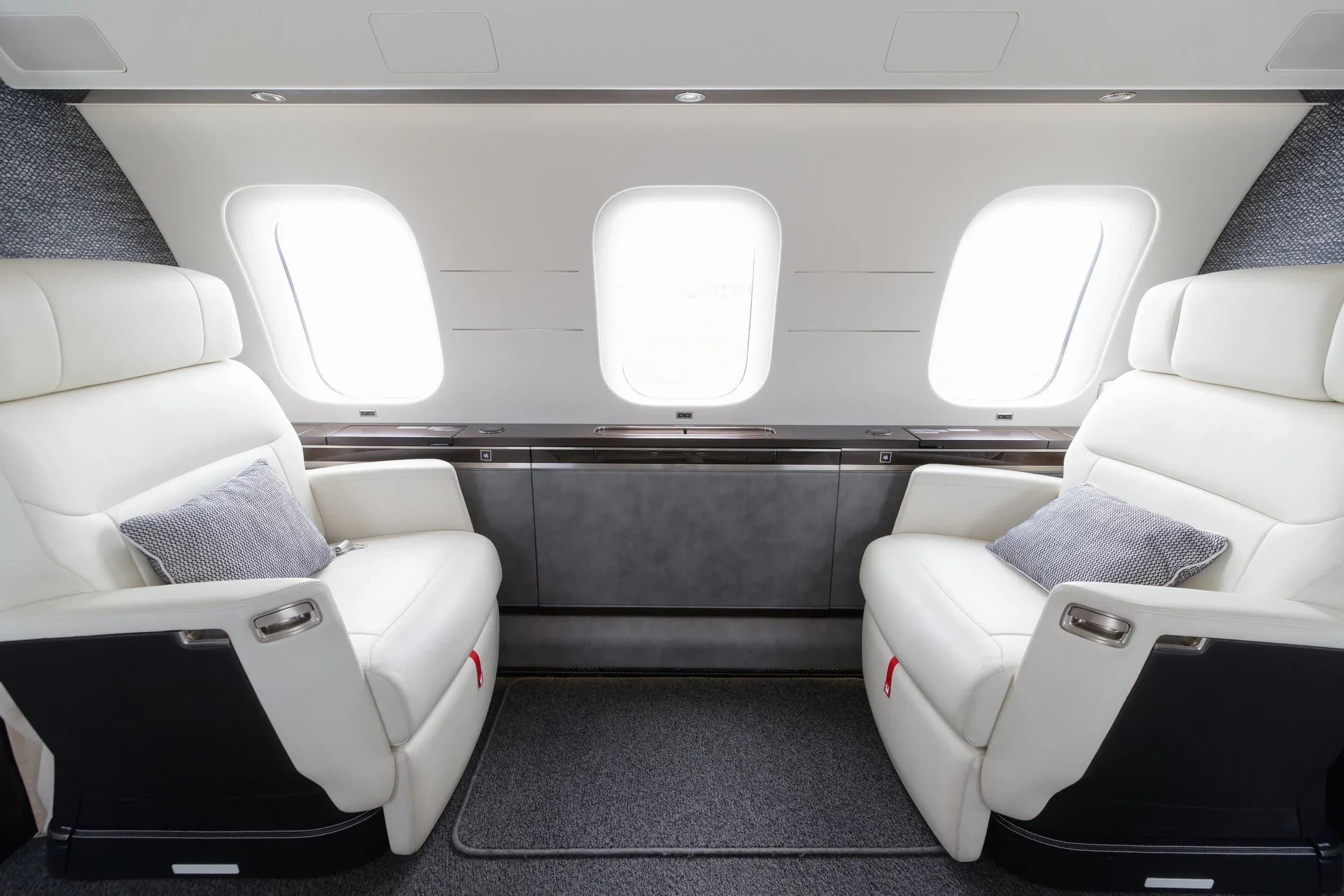 Two plush white leather seats facing each other in a private jet cabin, with large windows in the background.