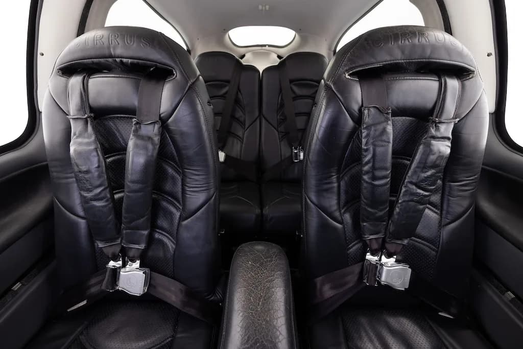 The black leather interior cabin of a Cirrus aircraft, showing two front seats with harnesses and two rear seats.